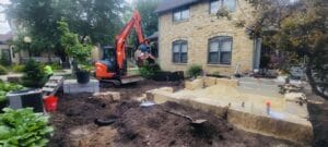 An orange mini excavator with grapple claw in motion prepares to pick up and move a 2'x4' mild steel bed that will be used for planting annual vegetables.