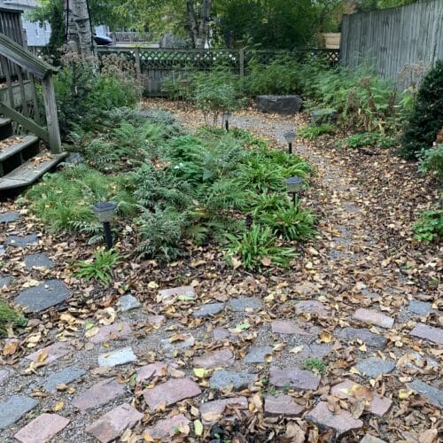 Landscaping Portfolio - Light Dark Landscape 13 A rustic cobblestone fire pit connected to a circular seating area via a winding gravel path in a small shaded backyard in the city of Minneapolis.