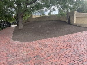 A steep slope of barren dry soil bounded by a block-long public walk and a tall retaining wall in a commercial pedestrian zone in the City of Minneapolis.