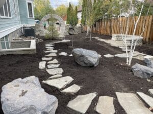 An empty side yard in the Kenwood Ave Neighborhood of Minneapolis has been transformed into a woodland retreat with the addition of newly planted birch trees, large gray boulders and a buff stone stepper path.